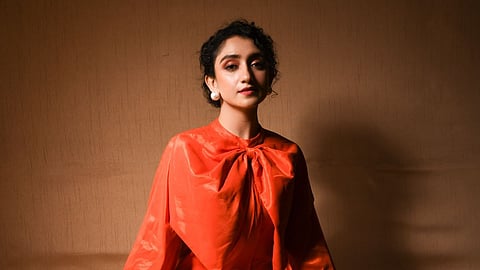 Sanjeeta in a silk dress in vibrant tangerine orange with subtle metallic sheen, bubble sleeves and oversized statement collar bow by label Suravika S