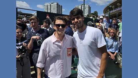 Tom Holland in pink shirt standing next to Carlos Alcaraz in a white shirt