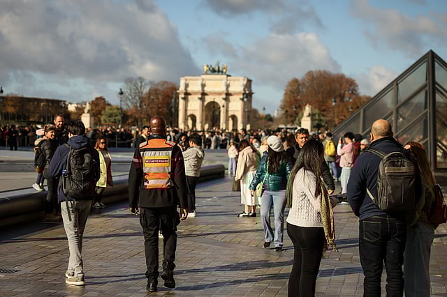 A member of a private security company, center, and visitors walk in the courtyard of the Louvre museum on Sunday