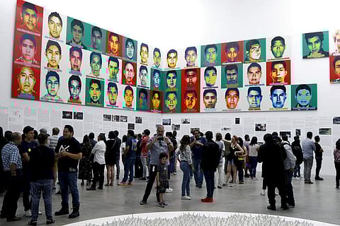 People stand under the portraits of 43 college students who went missing in 2014 in an apparent massacre, by Chinese concept artist and government critic Ai Weiwei. (AP Photo/Claudio Cruz)