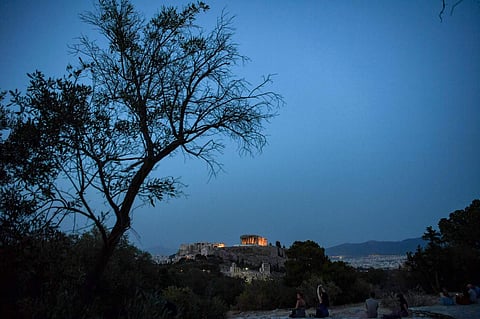 People sit on a hill facing the ancient Temple of Parthenon atop the Acropolis hill in Athens (AFP/ARIS MESSINIS)
