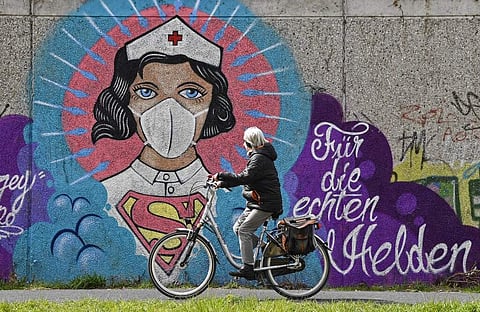 A file picture of a woman cycling past a coronavirus graffiti by street artist 'Uzey' showing a nurse as Superwoman in Hamm, Germany. (AP Photo/Martin Meissner)