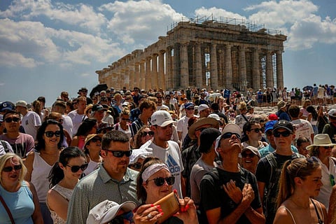 Atop the Acropolis ancient hill, tourists visit the Parthenon temple, background, in Athens, Greece