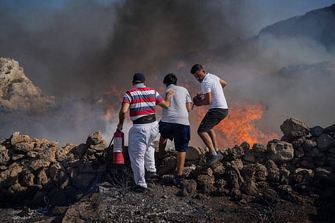 Local residents try to extinguish a fire, near the seaside resort of Lindos