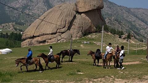Tourists enjoy horseback riding near the iconic Turtle Rock outcrop at the Terejl National Park outside Ulaanbaatar, Mongolia