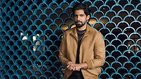 Actor Prabhu Mundkur stands in front of a jaali pattern wall looking straight into the camera