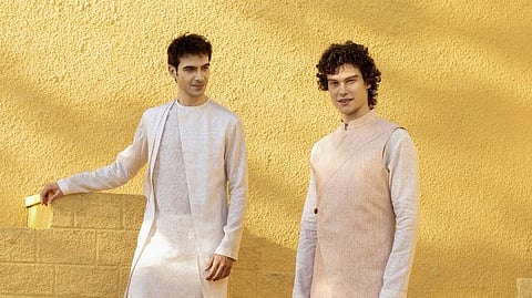 Two male models are seen posing in contemporary ethnic ensembles from PN Rao’s Linencraft against a bright wall