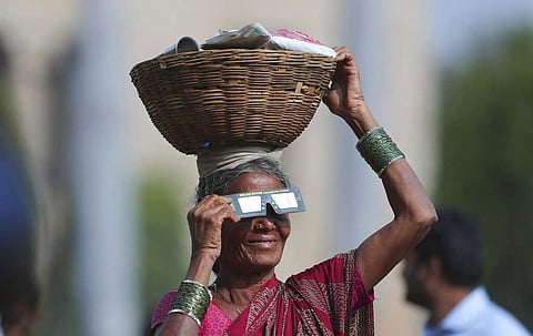 A roadside vendor holds a special filter and watches a partial solar eclipse in Hyderabad, India. (AP Photo/Mahesh Kumar A)