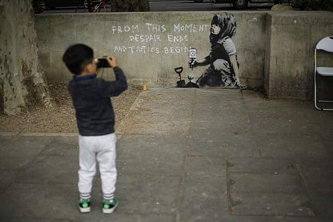 A young boy points towards a piece of street art believed to be by street artist Banksy where Extinction Rebellion climate protesters set up a camp in Marble Arch, London. (AP Photo/Matt Dunham)