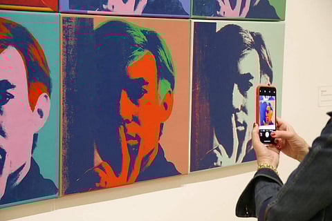A woman records one of a series of self-portraits at the exhibition, 'Andy Warhol _ From A to B and Back Again', in San Francisco. (AP Photo/Eric Risberg)