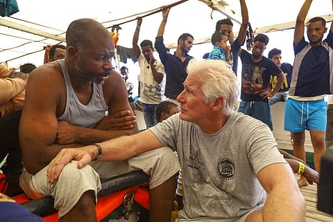 Actor Richard Gere talks with migrants aboard the Open Arms Spanish humanitarian boat, which has been carrying 121 migrants for a week in the central Mediterranean. (AP Photo/Valerio Nicolosi)