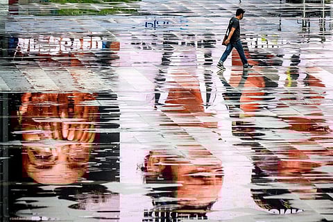 Bangkok: A man wearing a face mask, amid concerns over the spread of the coronavirus, walks between puddles reflecting advertisement screens on an empty square in Bangkok. (AFP/Mladen ANTONOV)