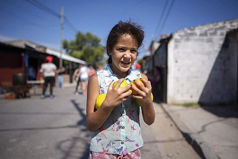 Buenos Aires, Argentina: Laila, 9, walks home with an armful of oranges she received at a soup kitchen, on the outskirts of Buenos Aires. (AP Photo/Victor R Caivano)