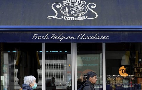 A woman in a face mask walks by the closed Leonidas chocolate shop in Antwerp, Belgium. (AP Photo/Virginia Mayo)
