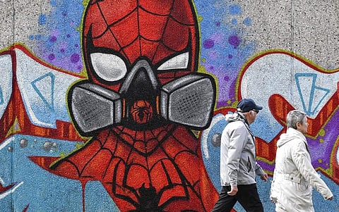People walk past a coronavirus graffiti by street artist 'Uzey' showing Spiderman with a protection mask on a wall in Hamm, Germany. (AP Photo/Martin Meissner)