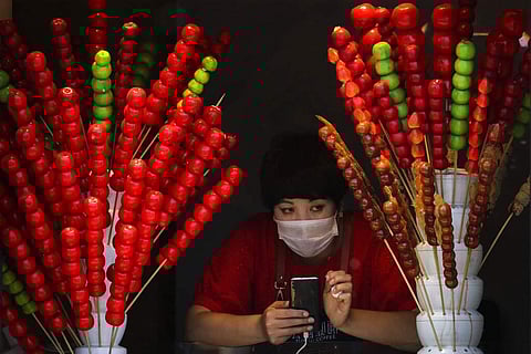 A vendor wearing a face mask looks out of her store selling sugar-coated haws on a stick in Beijing, China. (AP Photo/Andy Wong)