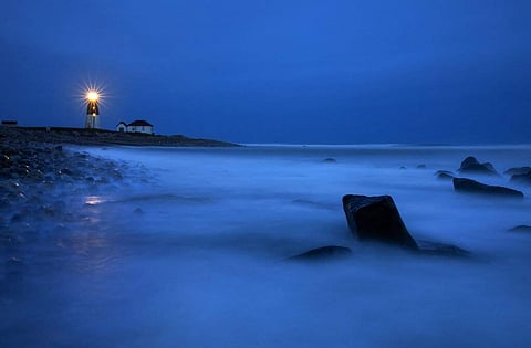 Waves wash over rocks as a beacon of light shines across the rocky shore from the Point Judith Lighthouse in Narragansett, Rhode Island. (AP Photo/David Goldman)