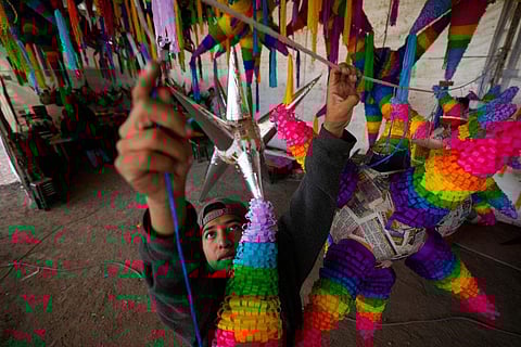 In frame: A worker hangs the most traditional style of 'piñata,' a sphere with seven spiky cone