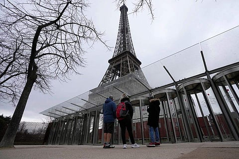 In frame: Visitors stand at the closed gates leading to the Eiffel Tower